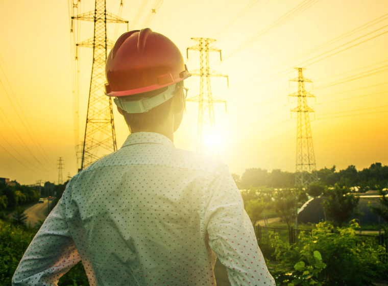 an electrician looking at three electrical towers during sunset